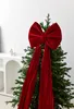 A large red velvet bow is placed on top of a decorated Christmas tree. Podgląd zdjęcia produktu
