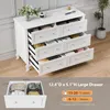 A white dresser with several drawers open, displaying folded clothes and a small decorative plant on top. Voir les images du produit