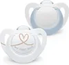 Two NUK pacifiers are shown against a white background. One pacifier is in the foreground and has a heart and text "MY FIRST NUK" printed on it. The other pacifier is in the background and has a light blue rim. Náhľad obrázku produktu