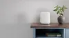 A white Orbi router sits on a wooden shelf next to a vase with greenery. Náhled obrázku produktu