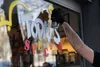 A person's hand wearing a black glove is spraying white lettering on a glass window. The lettering says "TODAY'S SPECIAL" in colorful letters. Produktbild-Vorschau