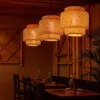A dimly lit restaurant interior with bamboo accents, featuring tables set with bottles and glasses, and three hanging pendant lamps. Náhled obrázku produktu