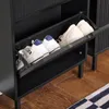 A close-up view of a black shoe cabinet with two shelves, each holding a pair of shoes. The cabinet has a ribbed texture on the sides and a metal pull-out drawer for shoes. Náhľad obrázku produktu