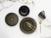 A flat lay of black and gold mandala-patterned dinnerware and cutlery on a white background, with decorative branches. Náhľad obrázku produktu