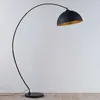 A black arc floor lamp with a gold interior shade stands against a white wall and light wood floor. Produktbild-Vorschau