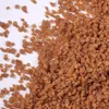 A pile of small, brown, granular food product, likely a topping or cereal, scattered on a white surface. Produktbild-Vorschau