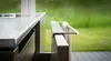 A close-up of a kitchen towel holder mounted on a cabinet, with a towel hanging on it. The background is a blurred green lawn. Produktbild-Vorschau