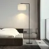 A modern floor lamp is positioned next to a bed in a bedroom. Produktbild-Vorschau