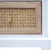 Close-up of a drawer front on a white cabinet, featuring a natural wood frame and a woven rattan insert with a gold knob. Anteprima dell’immagine prodotto