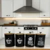 A set of four black storage canisters with wooden lids are displayed on a wooden countertop in a kitchen setting. Náhľad obrázku produktu