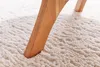 A close-up shot of a wooden table leg resting on a fluffy, cream-colored rug. Produktbild-Vorschau