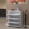 A white shoe cabinet with four open doors, a decorative bowl and vase on top, and an umbrella stand next to it, in a room with a painting on the wall. Produktbild-Vorschau