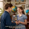 Two children are holding a miniature bookshop craft kit, with a globe and piano in the background. Náhled obrázku produktu