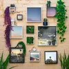A collection of framed pictures and plants arranged on a brick wall. Produktbild-Vorschau