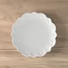A white plate with a decorative edge sits on a wooden surface. Voir les images du produit