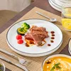 A table setting with a plate of steak and vegetables, a glass of water with lemon, and a bowl of soup. Voir les images du produit