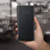 A hand holding a black phone case with a digital display showing the time and various icons. Produktbild-Vorschau