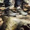 A person wearing hiking boots stands on a rock in a forest. Produktbild-Vorschau