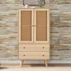 A wooden cabinet with cane doors and drawers against a brick wall. Produktbild-Vorschau
