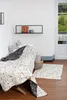 A child's bed with a blanket and pillows, a rug on the floor, and a shelf on the wall. Produktbild-Vorschau