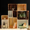 A collection of wooden crates stacked and arranged, some containing decorative items like vases, plants, books, and flowers. Produktbild-Vorschau