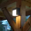 A modern black LED wall light is mounted on a wooden post, illuminating the surrounding wooden beams and structure. Podgląd zdjęcia produktu