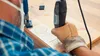 A person wearing a mask and gloves is using a Dremel rotary tool to engrave a wooden board. Produktbild-Vorschau