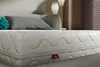 A close-up view of a mattress in a bedroom setting. Podgląd zdjęcia produktu