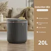A dark gray induction bin is placed on a wooden floor in front of a tufted beige sofa. The bin has a gold rim and a small circular button on its front. To the right of the bin, there is text describing its features and capacity. Produktbild-Vorschau