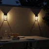 An outdoor dining table set at night, illuminated by wall-mounted lights. Produktbild-Vorschau