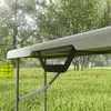 A close-up of a folding table in a grassy outdoor setting with trees in the background. Produktbild-Vorschau