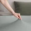 A hand is shown stretching a light gray fitted sheet. Produktbild-Vorschau