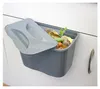 A dark gray hanging kitchen bin filled with food scraps, with its lid partially open. Produktbild-Vorschau