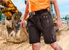A person wearing work shorts and an orange shirt stands in front of an excavator at a construction site. Anteprima dell’immagine prodotto