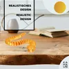 A 3D printed snake toy is placed on a wooden table next to an open book. The background shows a blurred interior scene. Voir les images du produit