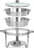 A disassembled stainless steel chafing dish set, including a glass lid, two food pans, and a fuel burner stand, arranged against a white background. Anteprima dell’immagine prodotto