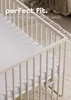 A close-up view of a white crib with a fitted sheet. Produktbild-Vorschau