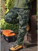 A person wearing camouflage pants and yellow work boots leans against a wooden post next to a toolbox. Voir les images du produit