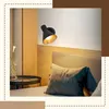 A close-up view of a black wall lamp with a gold interior, mounted above a bed with a headboard and pillows in a bedroom setting. Náhľad obrázku produktu