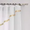 A close-up view of a white sheer curtain with a gold ribbon trim, hanging from a curtain rod. Produktbild-Vorschau