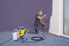 A man is kneeling and painting a wall with a spray gun. A paint sprayer machine is on the floor next to him. Náhled obrázku produktu