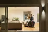 A couple sitting on a couch in a modern living room at night, with the interior illuminated by warm lighting. Produktbild-Vorschau