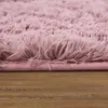 A close-up view of a fluffy pink rug with a wooden floor. Produktbild-Vorschau
