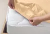 Hands are shown putting a beige fitted sheet onto a white mattress. Produktbild-Vorschau