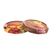 Two round metal jar lids with a printed design of fruits and vegetables on a wooden background. Voir les images du produit