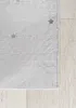 A close-up view of a rug with a subtle star pattern, placed on a light-colored wooden floor. Náhled obrázku produktu