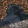 A close-up view of black landscape fabric with green and red grid lines, partially covered with wood chips and laid over a path of small stones. Produktbild-Vorschau