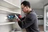 A man is using a Bosch cordless multi-cutter to make a cut in a shelf of a white cabinet. Podgląd zdjęcia produktu