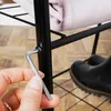 A hand is using an Allen wrench to assemble a black metal clothing rack. A black boot is visible in the background. Náhled obrázku produktu