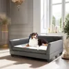 A dog is resting on a pet sofa in a well-lit room with large windows. Voir les images du produit